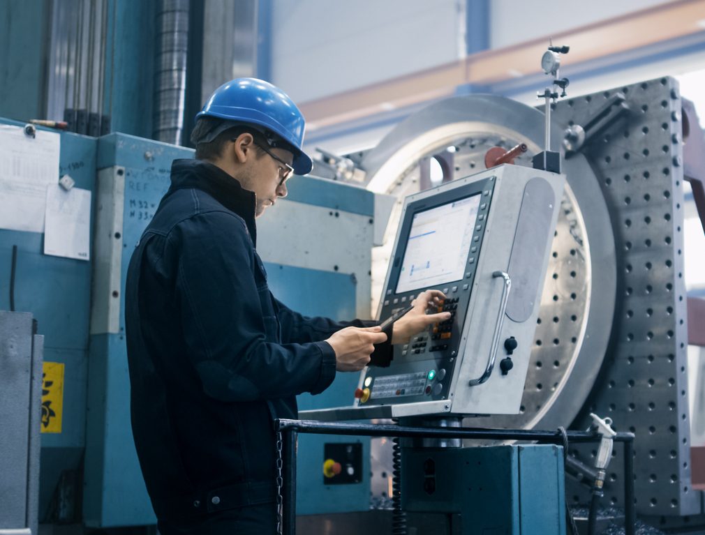 Factory worker programming a CNC milling machine with a tablet computer.